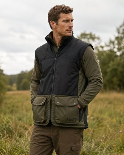 A man wearing a Reisto outdoor vest over an olive green long-sleeve shirt, standing in a grassy field under an overcast sky.